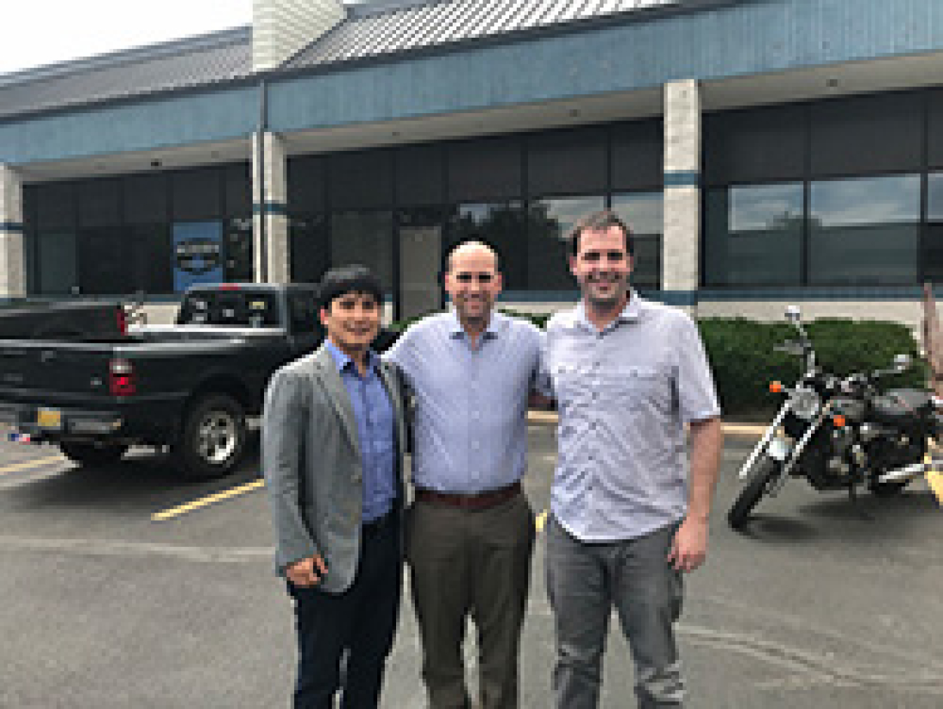 Three men smiling while standing outside.