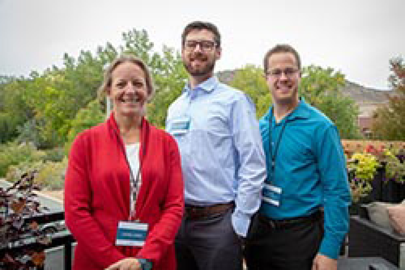 A woman and two men smiling while standing outside.