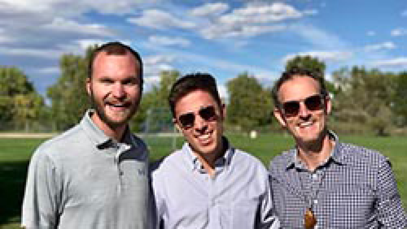 Three men smiling while standing outside.