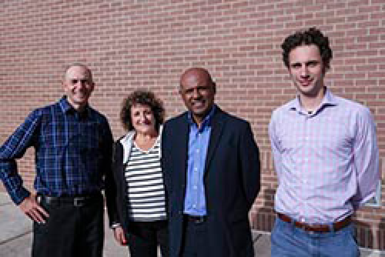 A woman and three men smiling while standing outside.