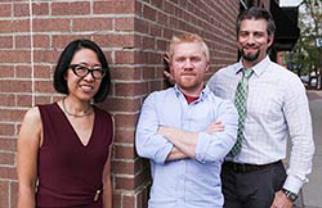 A woman and two men smiling while standing outside.