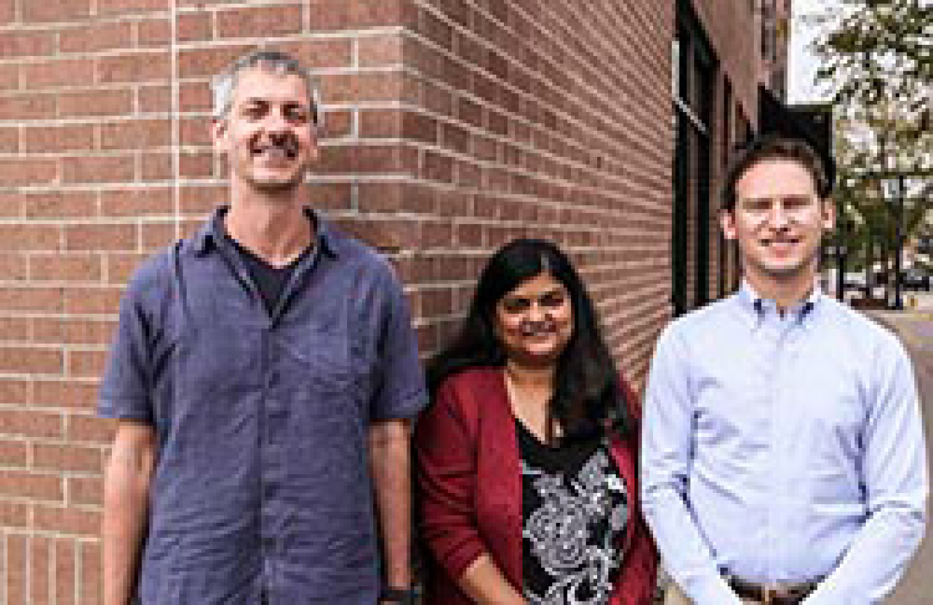 A woman and two men smiling while standing outside.