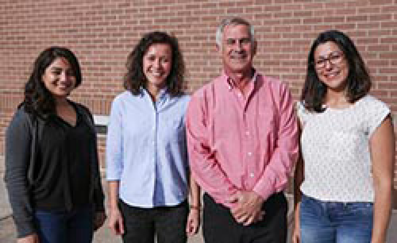 Three women and a man smiling while standing outside.