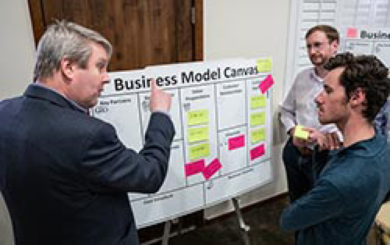 Three men having a discussion in front of a poster board.