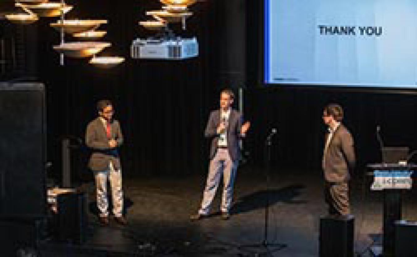 Three men presenting on stage.