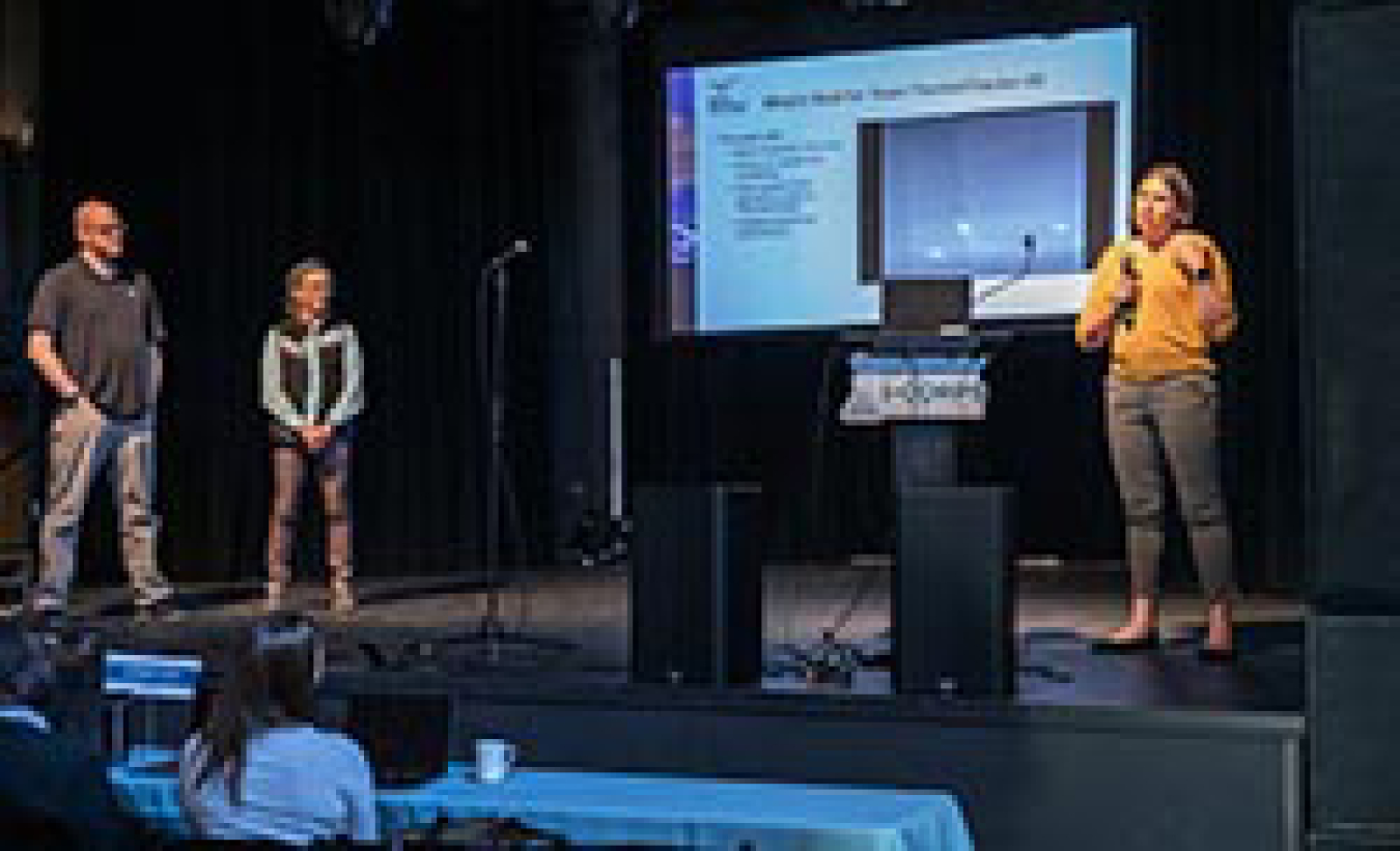 Three people presenting on a stage.