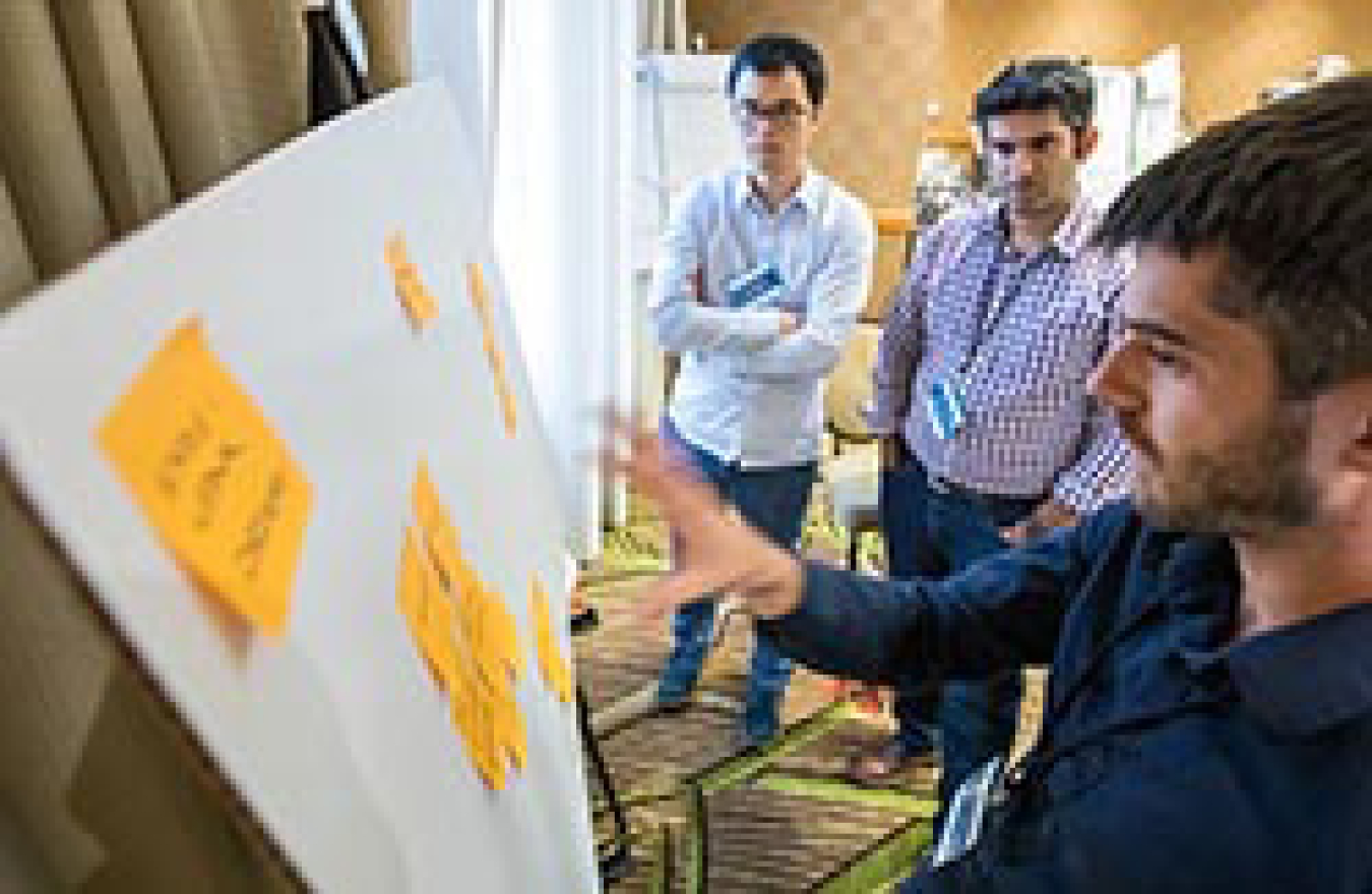 Two men examining a poster board with sticky notes. 