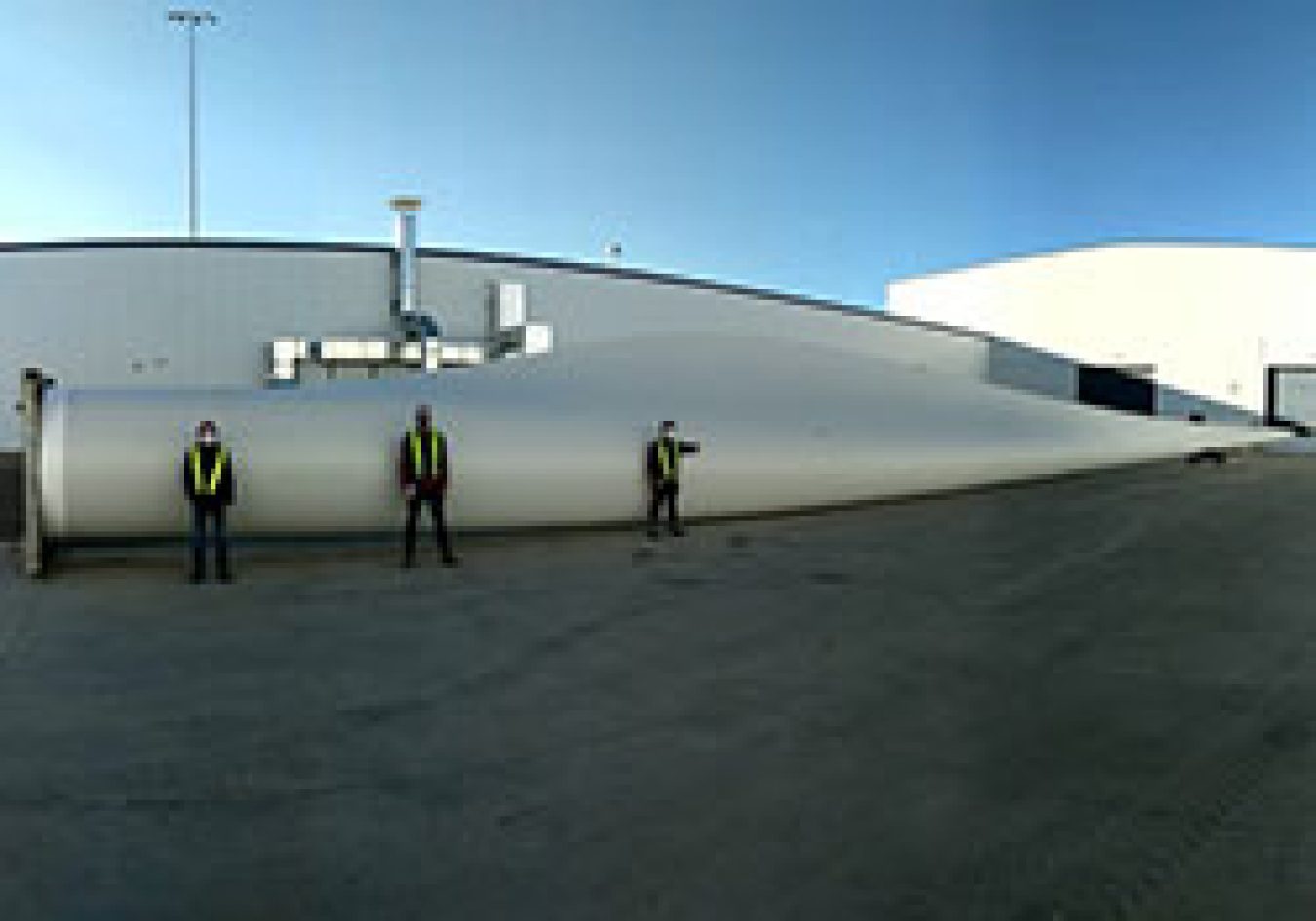 Three people standing outside in front of a wind turbine blade.