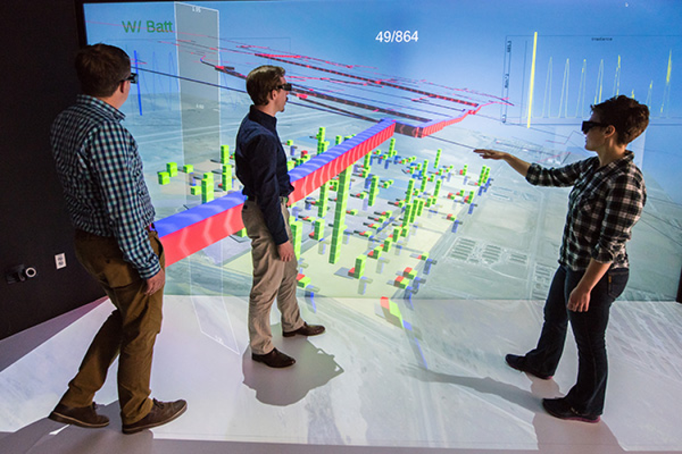 Three people standing in front of a large image board, looking at a 3D diagram.