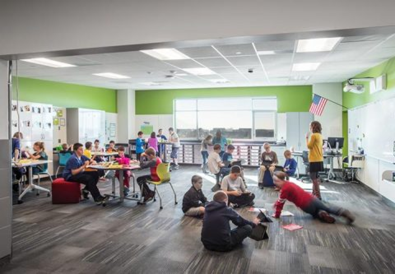 The inside of an elementary school classroom, with kids sitting in chairs and on the floor.