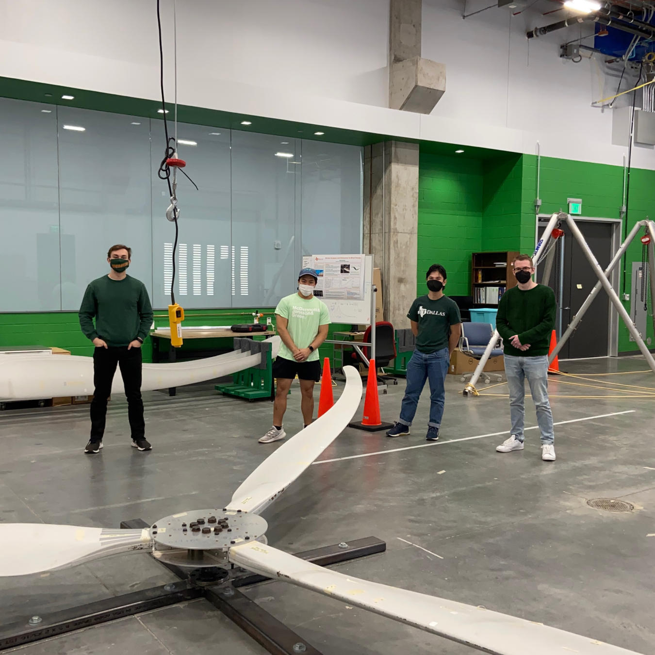 Team members of the University of Texas at Dallas collegiate wind competition stand around model wind turbines.