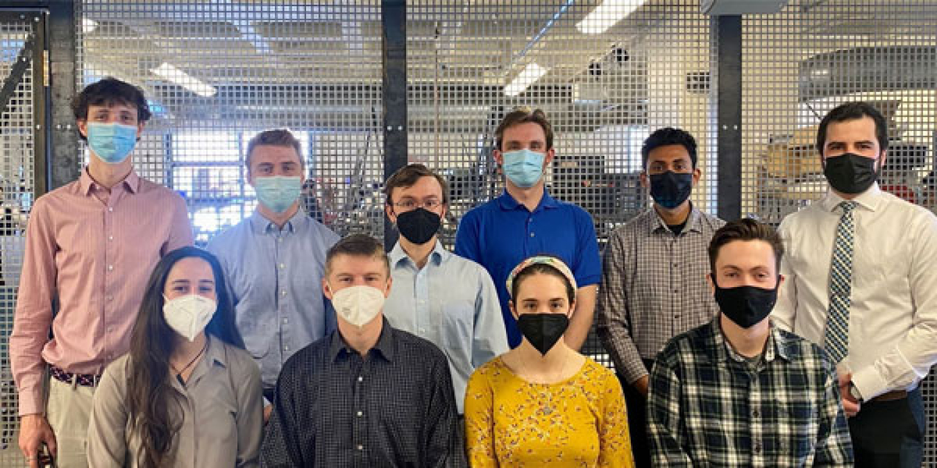 A group of young men and women wearing face masks in a laboratory or workshop setting.