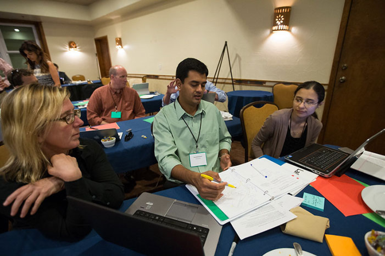 A team of two women and a male work on a project together at a table covered with papers and laptop computers.