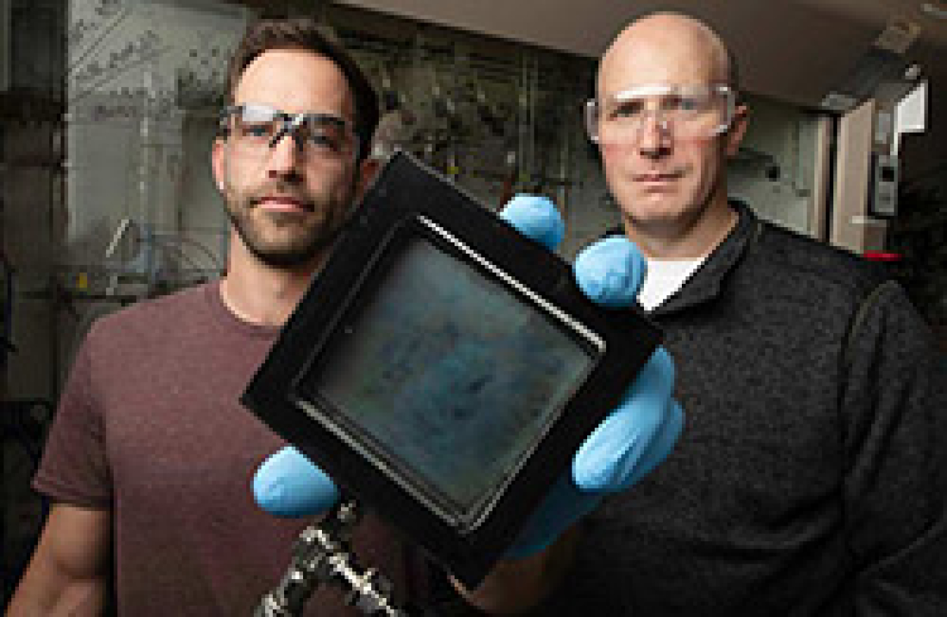 A male researcher holds a square-shaped sample of the SwitchGlaze technology alongside another male.