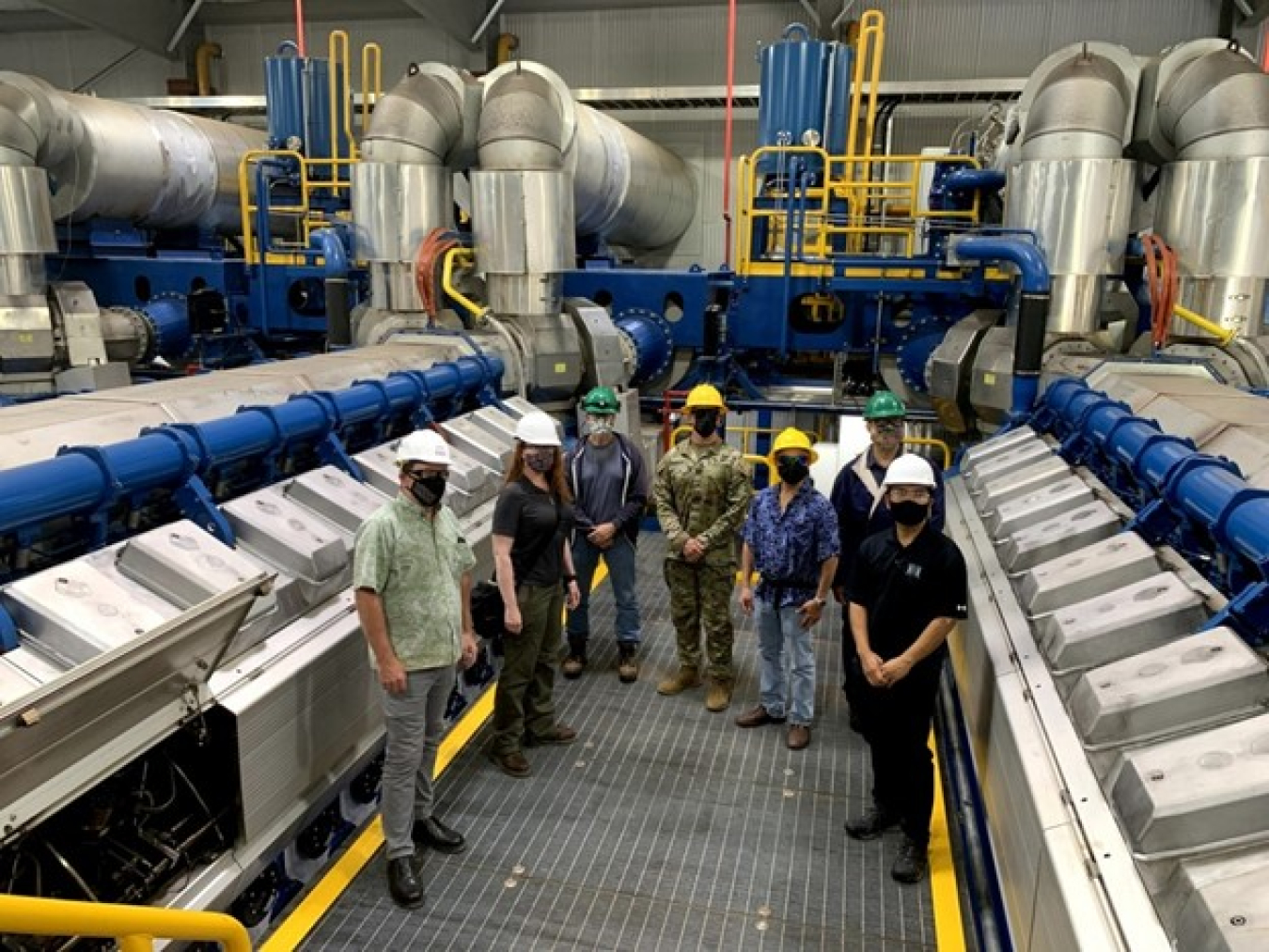 A group of individuals wearing safety hats and face masks in a power plant.