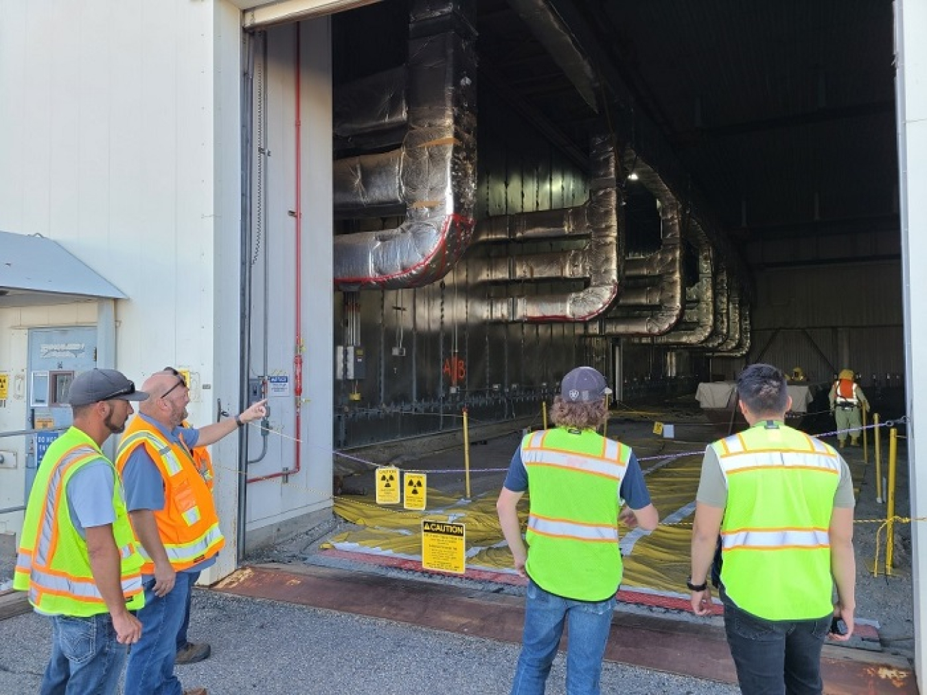 Idaho Environmental Coalition project manager Mark Henderson, shown here in the orange vest, second from left, talks to new crew members about the intricacies of removing asphalt from Transuranic Storage Area-Retrieval Enclosure.