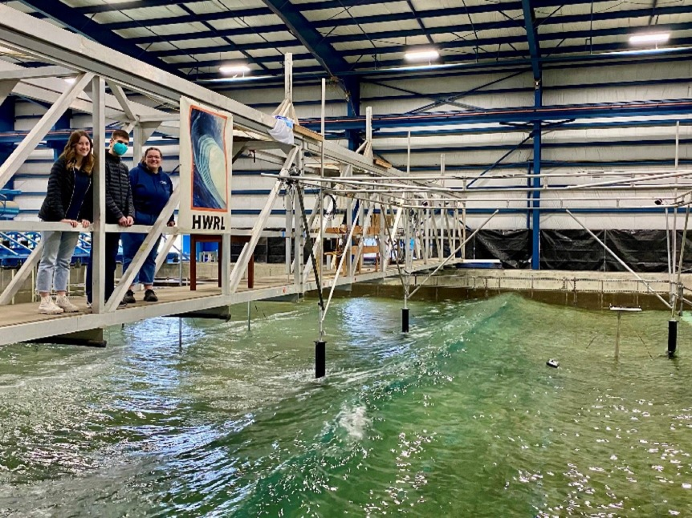 Three people stand on a bridge over a pool in a testing facility.