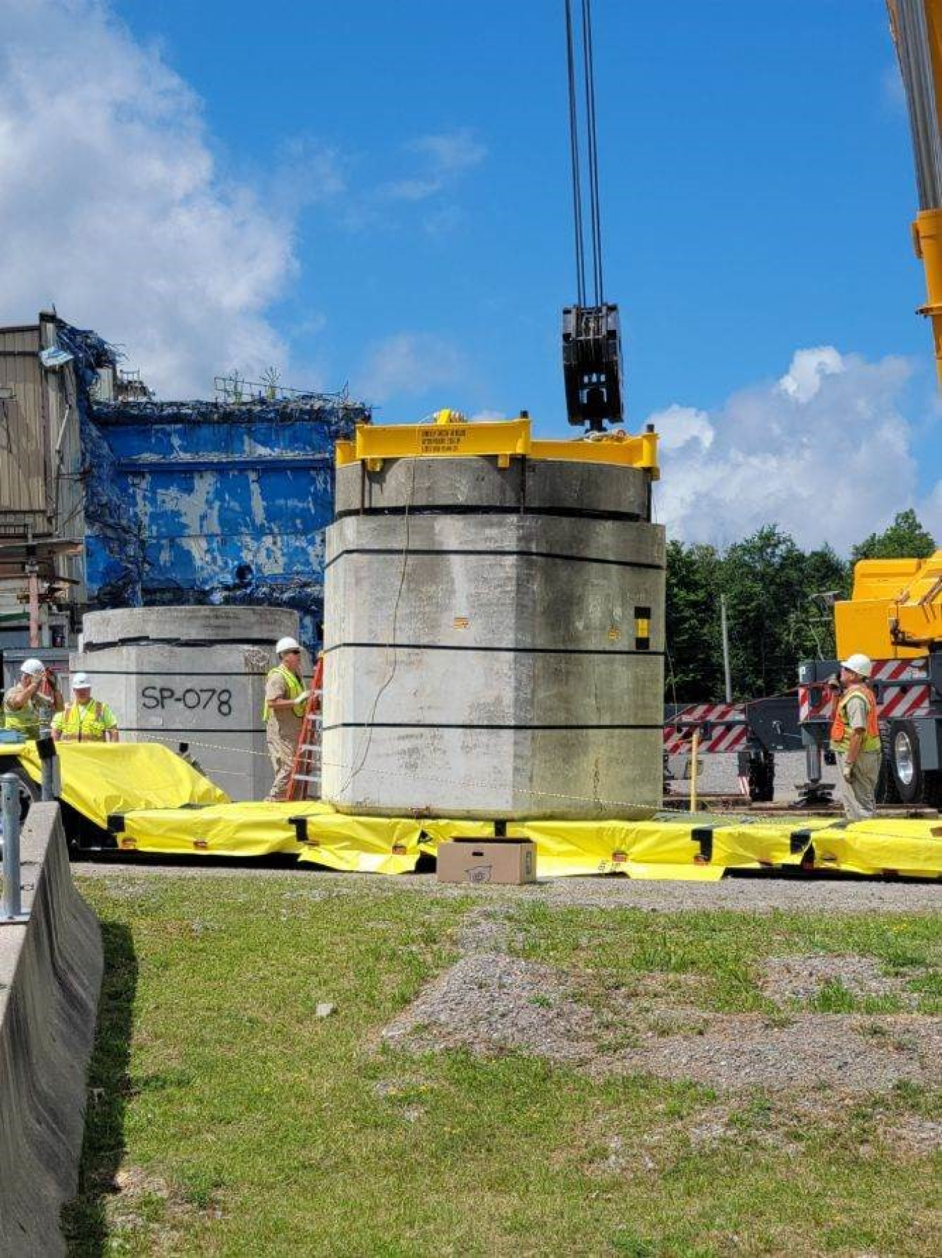 Using a 360-ton crane, crews lift a concrete shielded container of waste from its location near the Main Plant Process Building onto a flatbed trailer. A total of eight concrete shielded waste containers will be overpacked and shipped offsite for disposal.