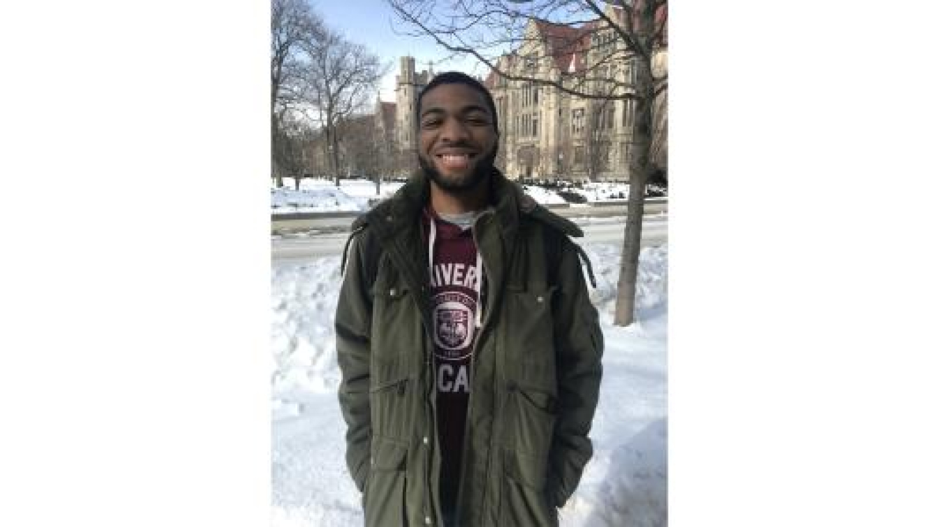 Young man in army green jacket stands on snow-covered college campus grounds. He has a great smile.