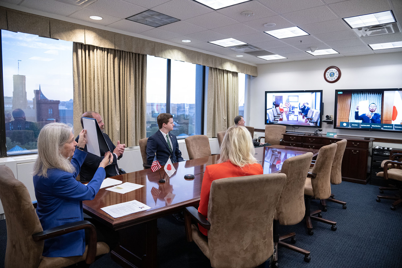 NNSA's Jill Hruby holds up a signed version of the MOU as her Japanese colleague, on video, does the same.