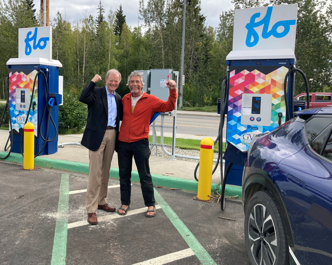 AEO Director George Roe, left, stands with his celebratory fist in the air with an early adopter. They both stand next to an Electric car.