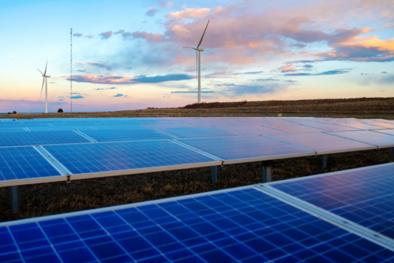 Solar panels in the foreground with wind turbines in the background.