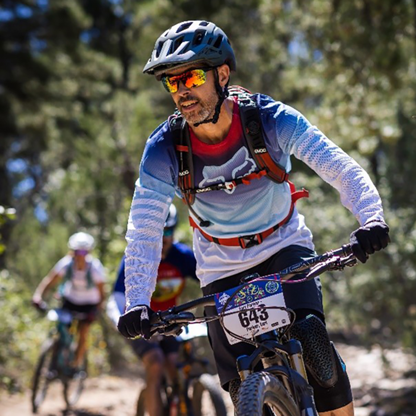 Parker rides a mountain bike in a race on a course with other bikers behind him.