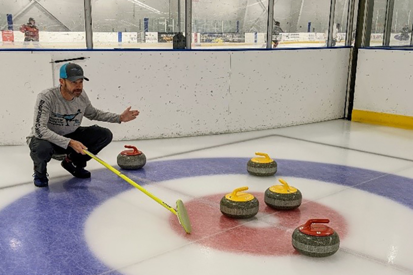 Parker stands in front of curling stones at an ice rink. He is crouching on the ice and holding a curling broom.