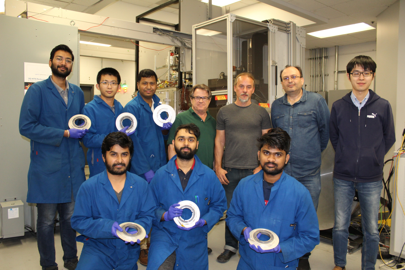 UH graduate students are holding spools of long superconductor wires 