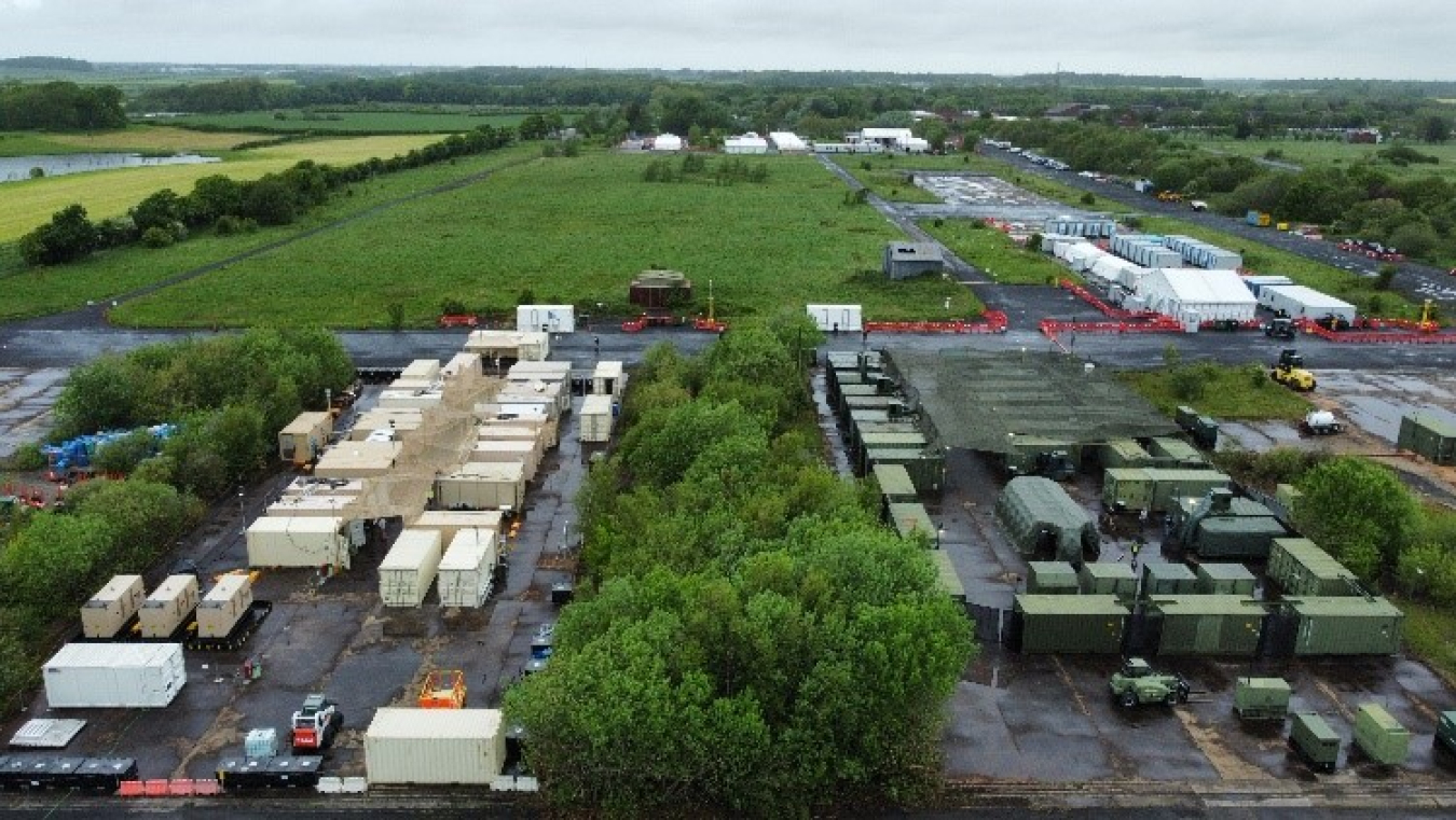 An aerial view of dozens of shipping containers among trees. The containers on the left are white and the ones on the right are green.