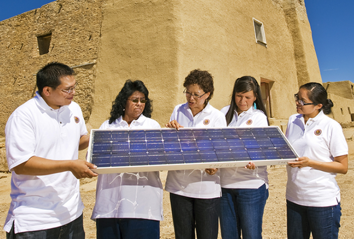 Five people wearing white shirts hold and look at a solar panel