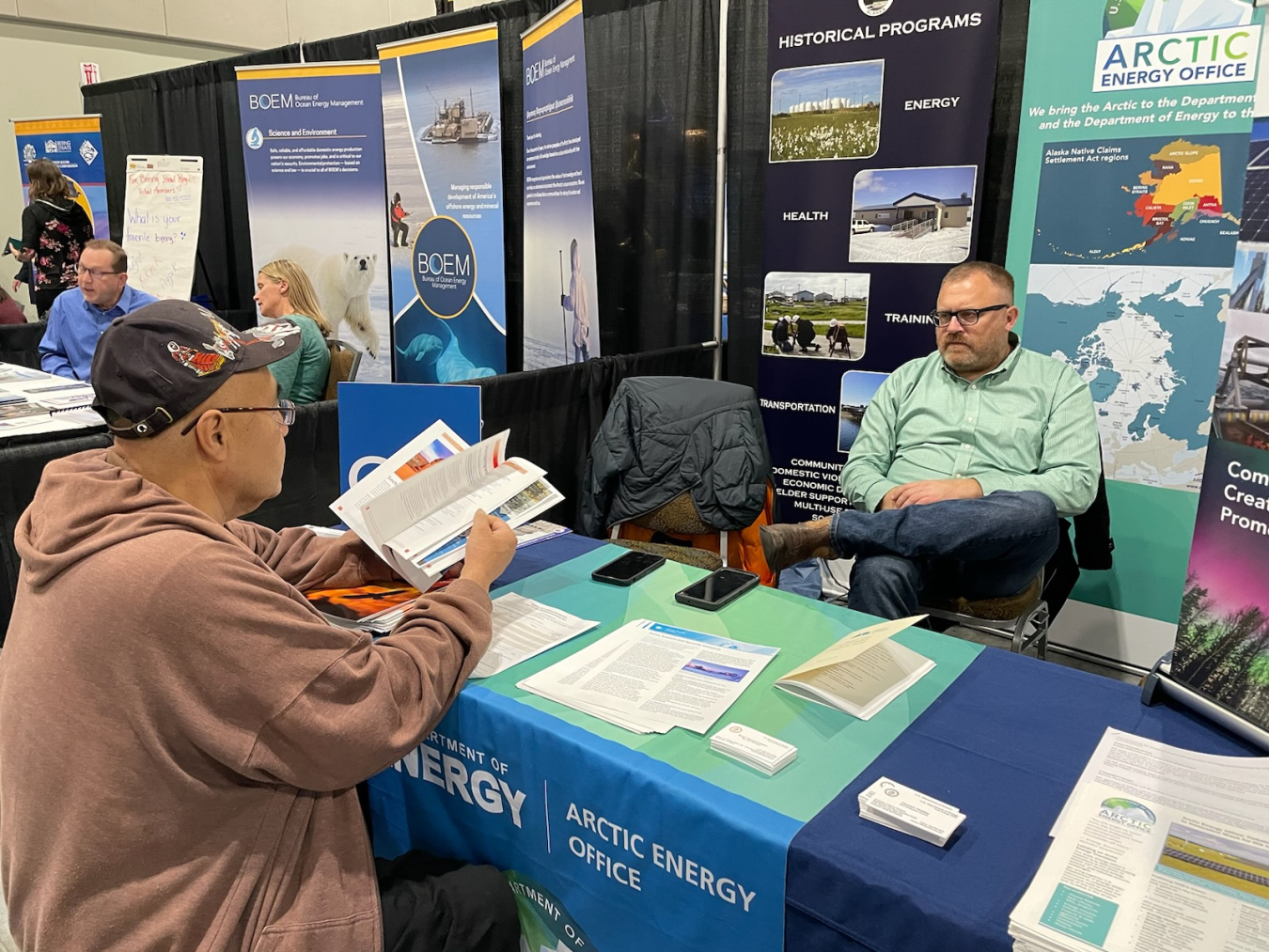 Givey Kochanowski sits in the Arctic Energy Office booth and talks to an Alaskan Native stakeholder.