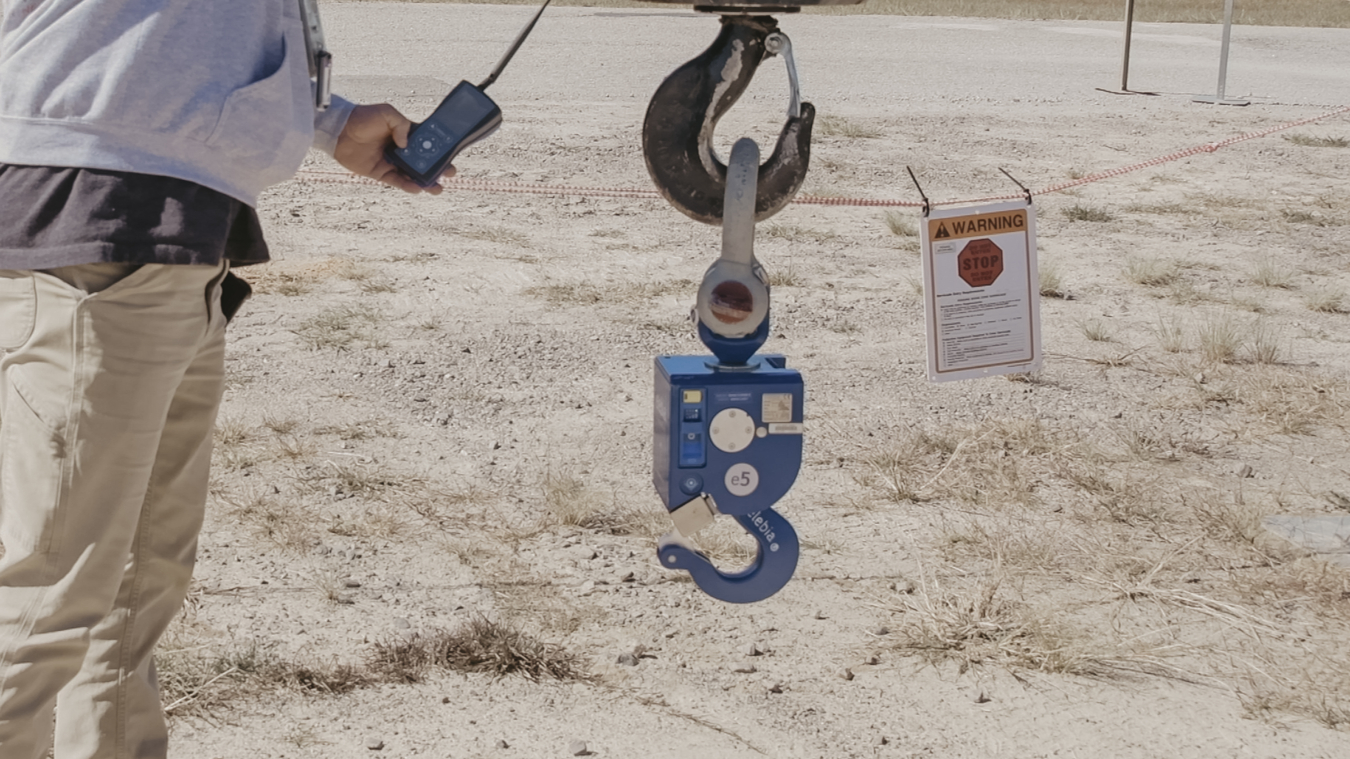 An operator holds a remote control that operates the remote release hook. The hook allows riggers to place low-level radioactive waste in a slit trench with less potential for contamination while reducing radiological dose exposure and eliminating fall protection risk.