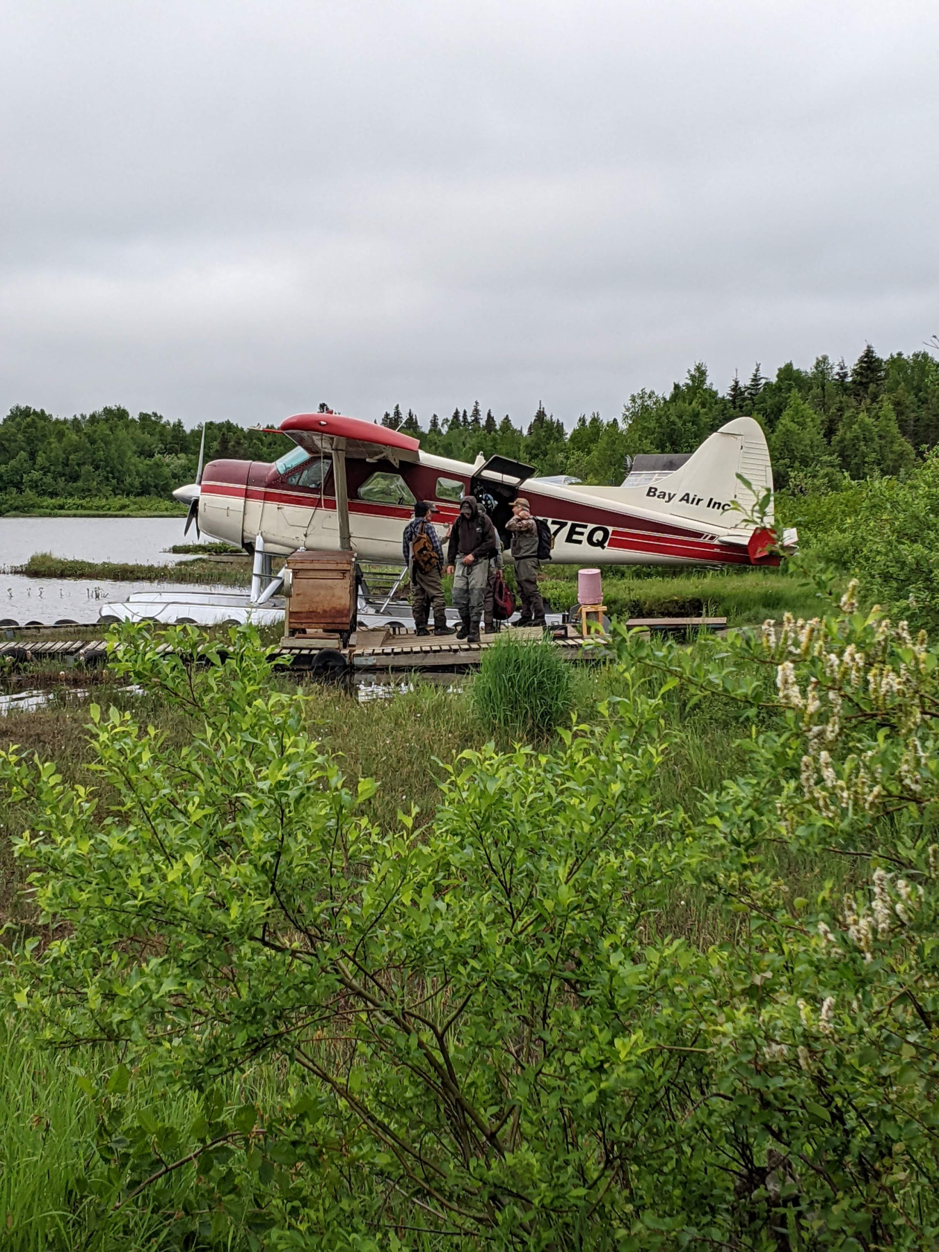 People stand next to a seaplane on the banks of a river.