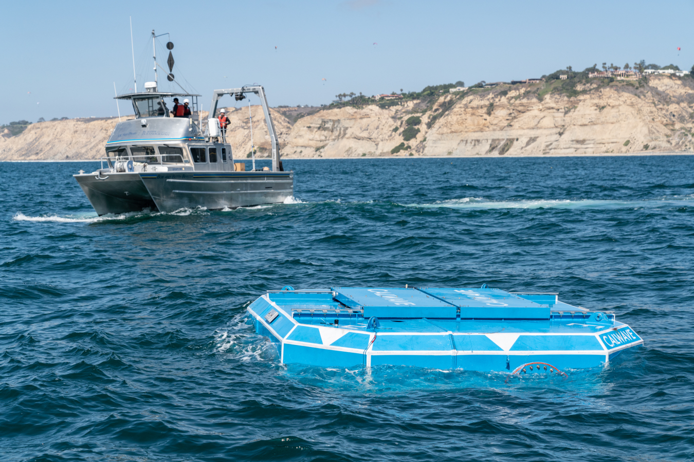 The hexagonal blue xWave floats near the ocean surface as a boat movespast.