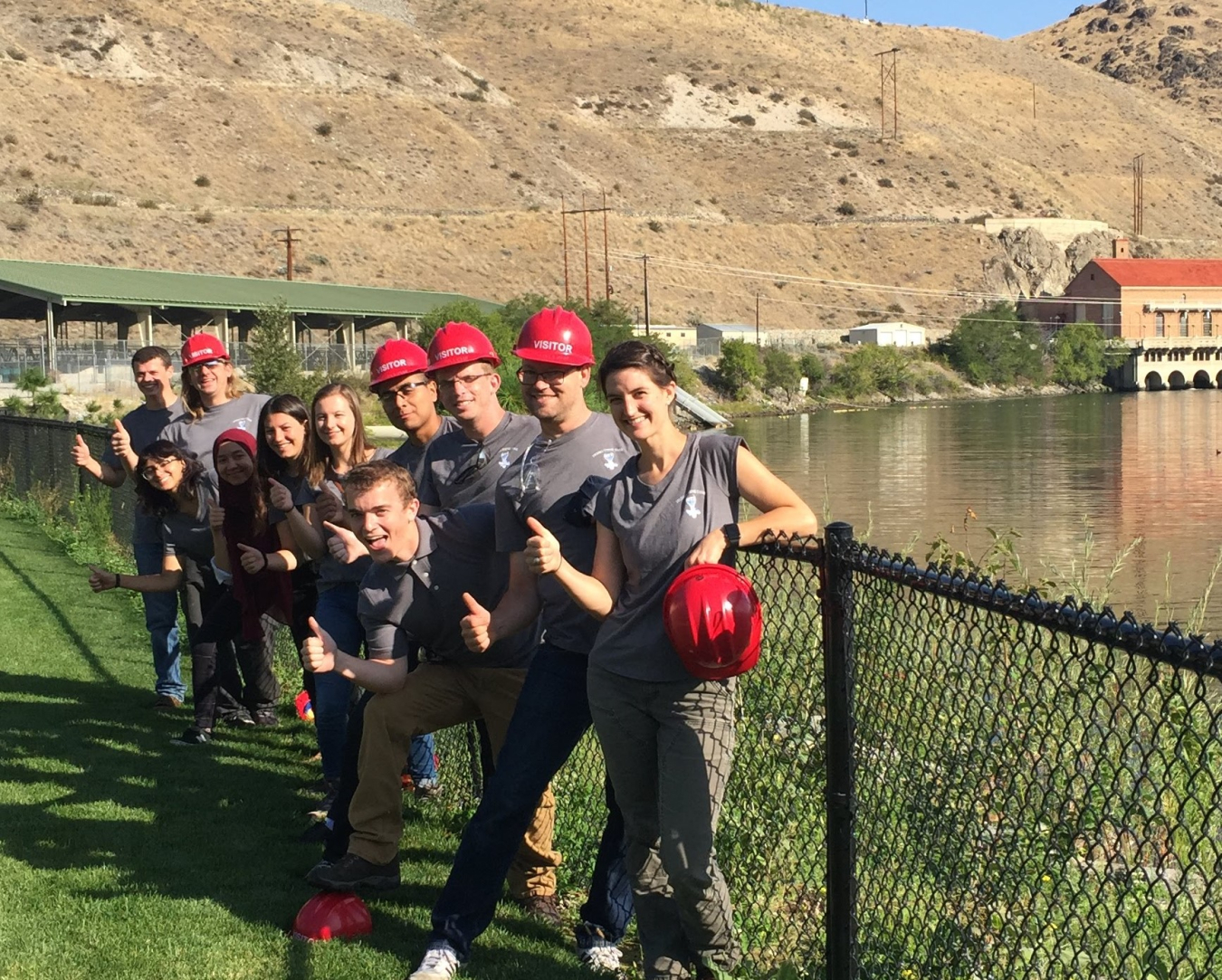 A group of students standing near a body of water and a hydropower dam