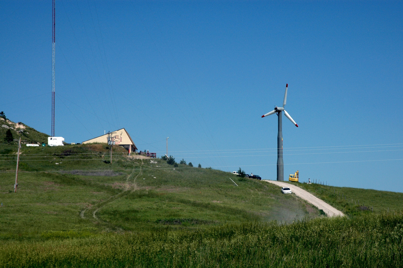 A wind turbine on a rural hill next to a building.