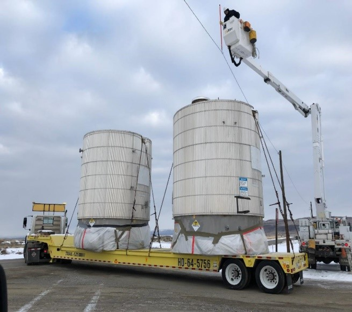 Electrical lineworkers with Hanford Mission Integration Solutions carefully lift overhead power lines to allow a trailer hauling empty tanks to Hanford’s landfill to pass.