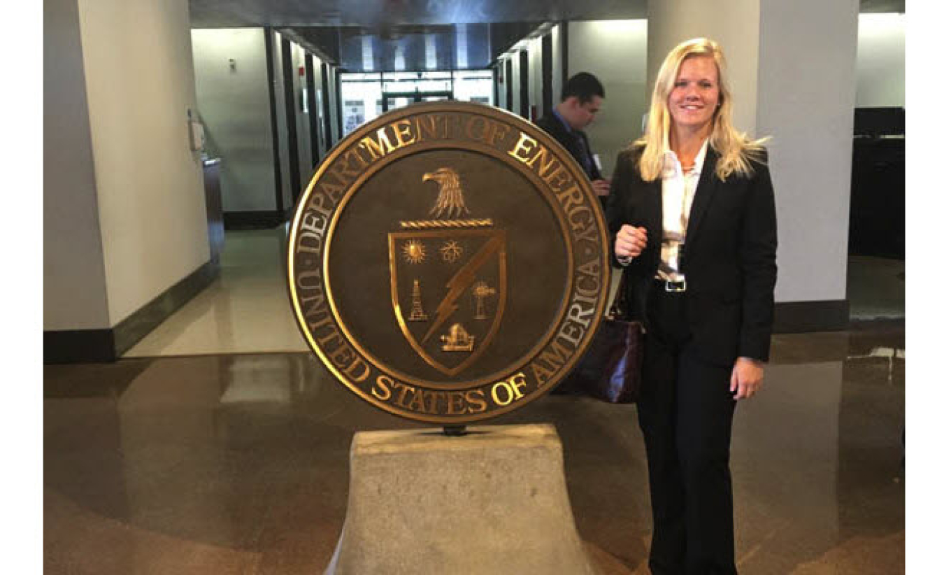 Caroline Quanbeck standing beside bronze DOE Seal