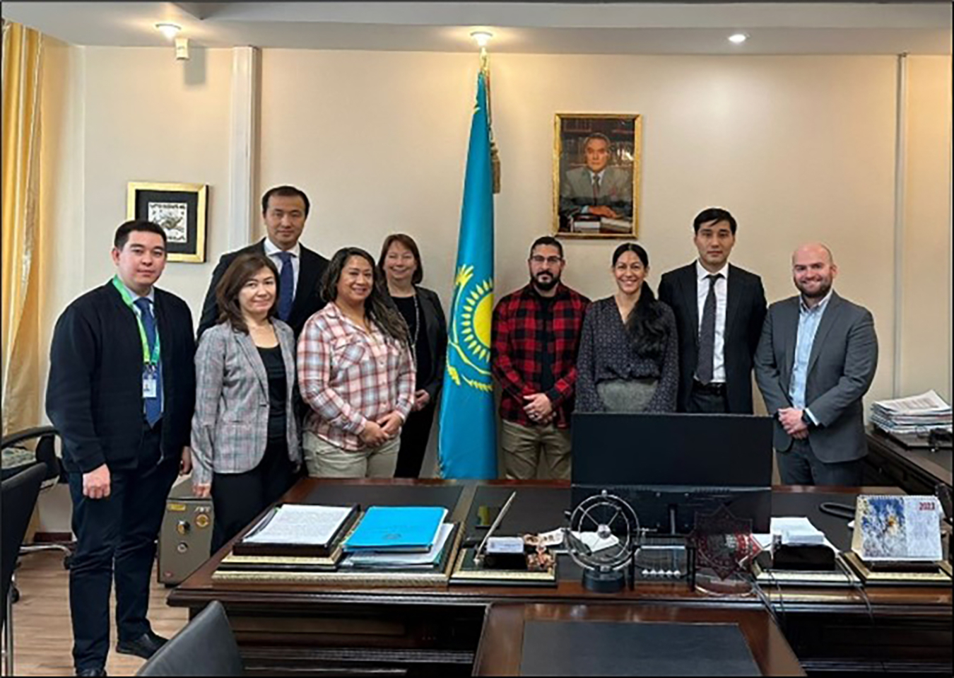 A group of people pose in front of the flag of Kazakhstan.