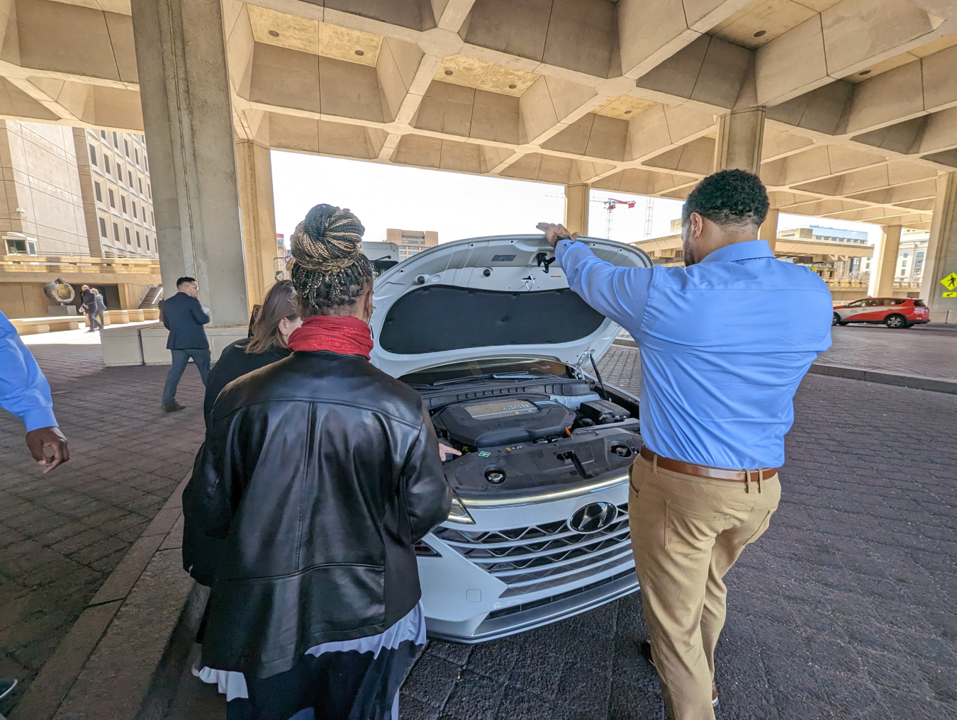 Three people stand in front of a car. The hood of the car is up to show the fuel cell engine. 