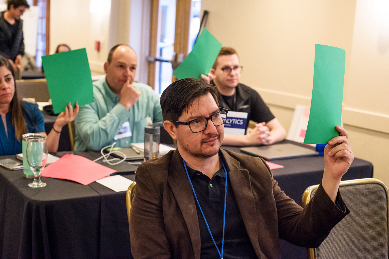 A group of four people sit at tables and hold up green pieces of paper.