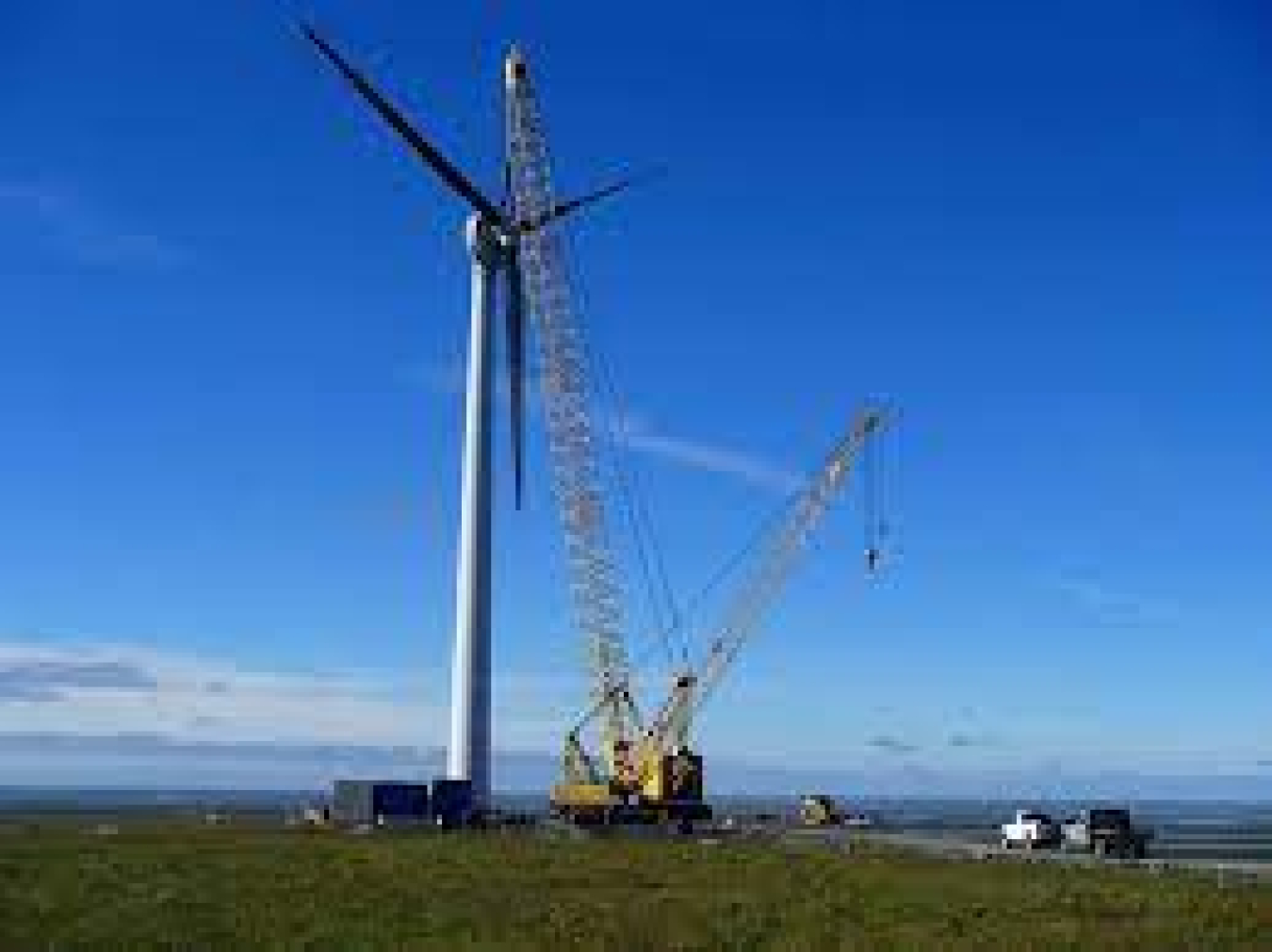 A wind turbine is disassembled by a crane and crew of workers.