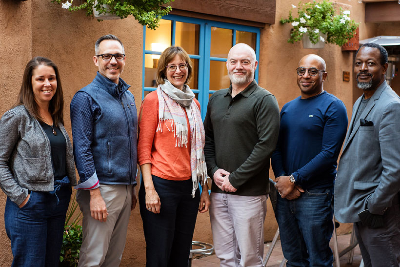 A group of six people stand together for a photo on an outdoor patio.