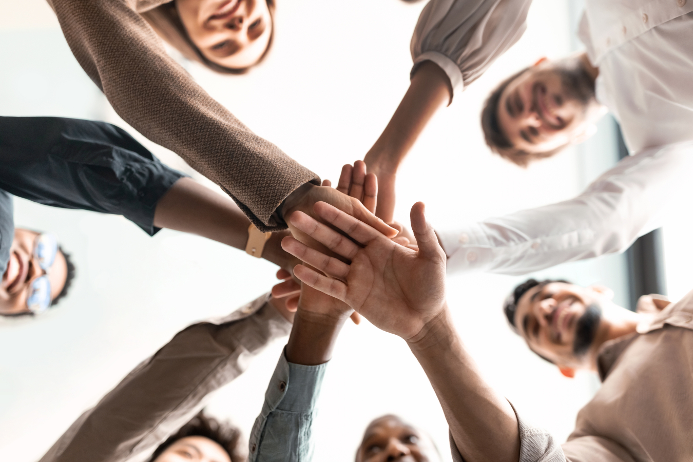 A diverse group of smiling people putting their hands together, standing in circle