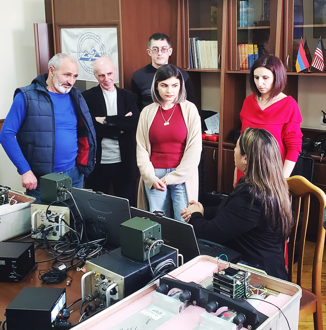 A group of people listen to a woman explaining a computer system.