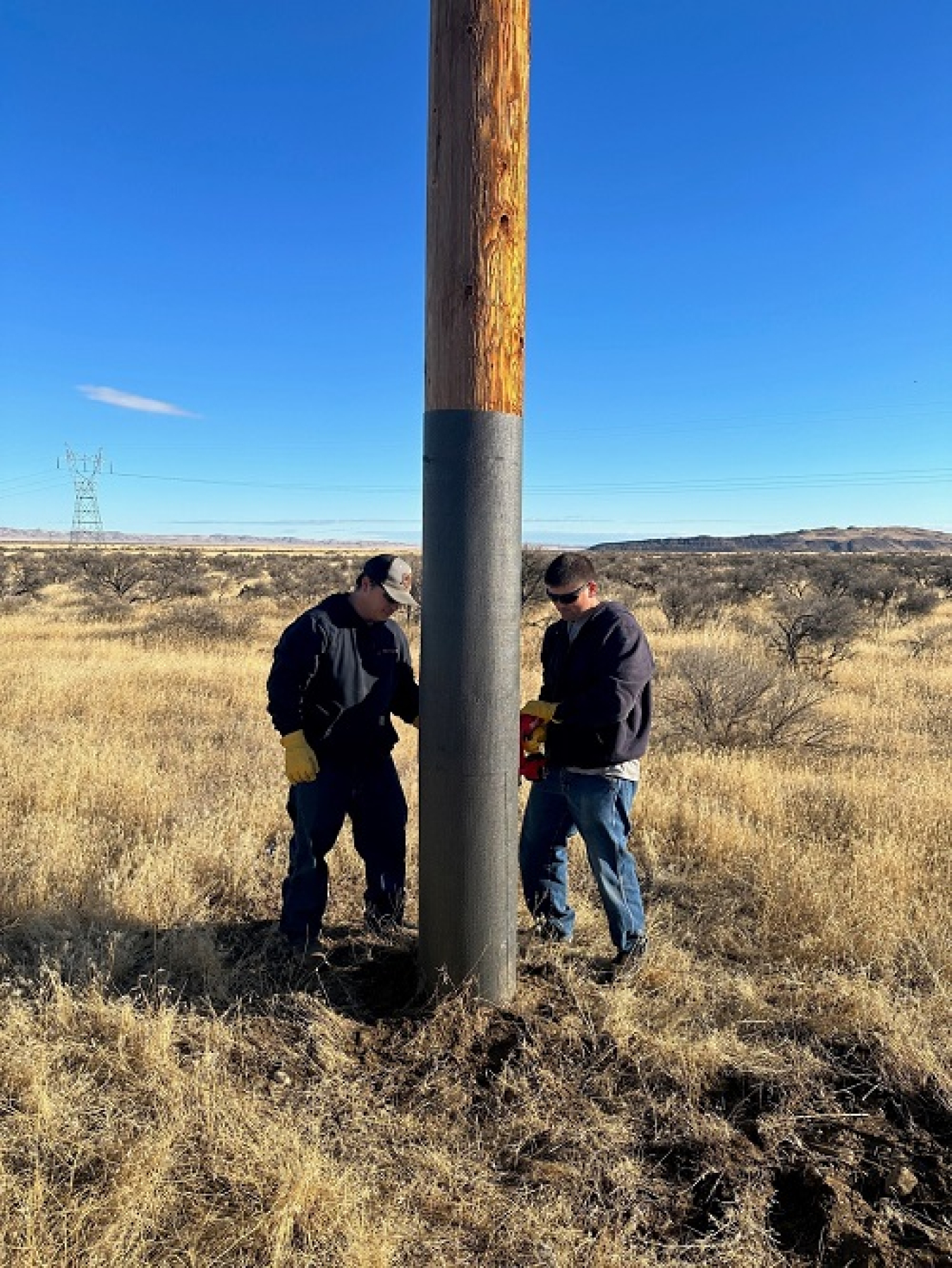 Hanford Mission Integration Solutions employees Riley Downs, left, and Britt Farnsworth apply fireproofing material on utility poles to help prevent any potential fire damage.