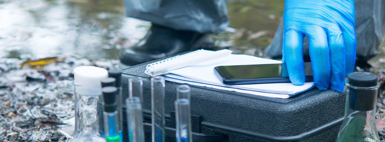 A close up of a scientist or researcher’s hand taking test tube samples from a river.