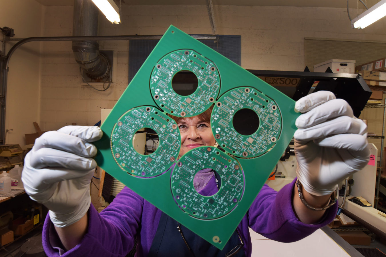 A woman holds up a circuit board. The Circuit Shop in Albuquerque, NM is a small, woman-owned business that contracts with Sandia National Laboratories.