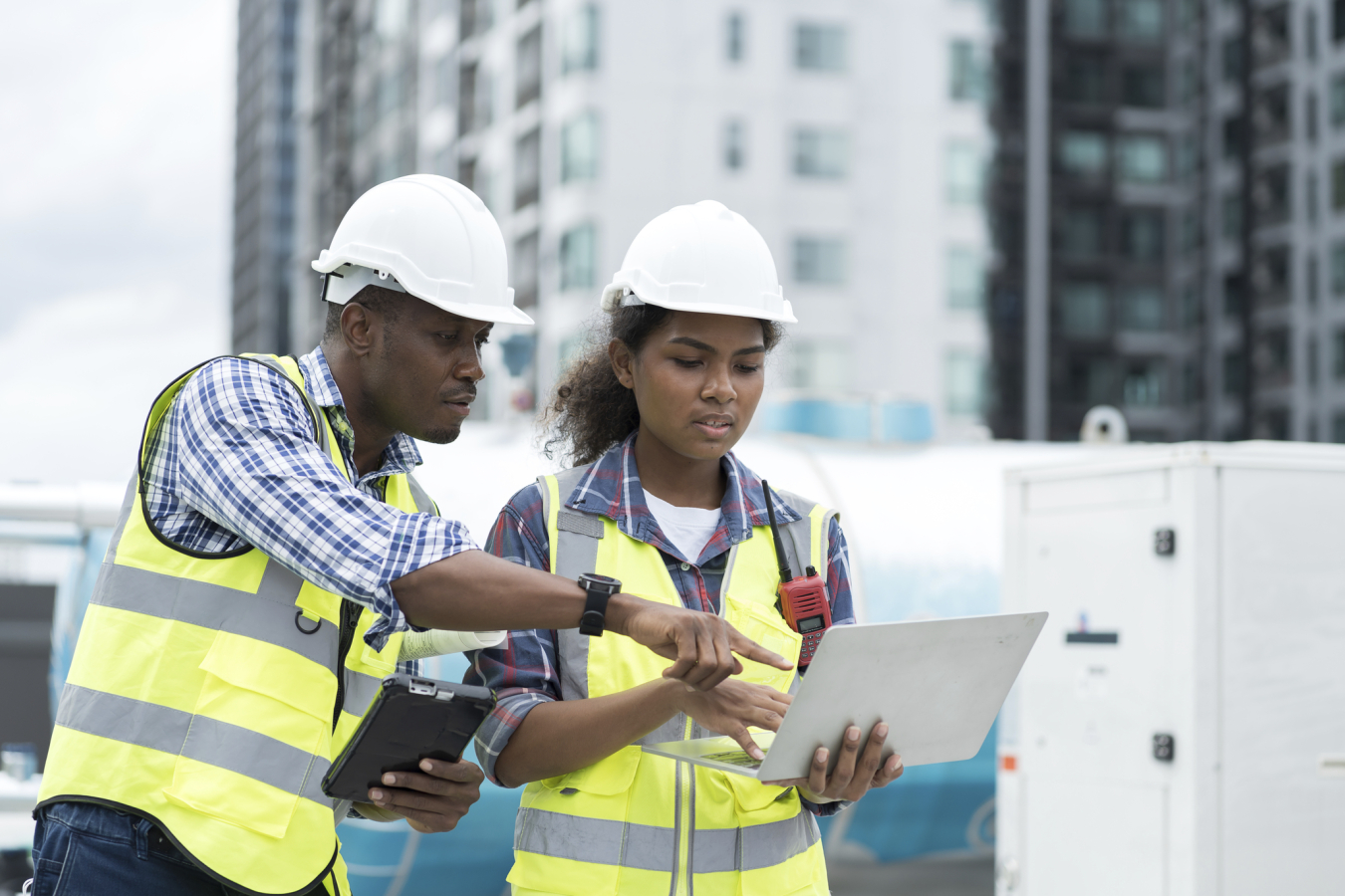 Construction workers standing on top of a building pointing, an experienced worker is mentoring a newer worker